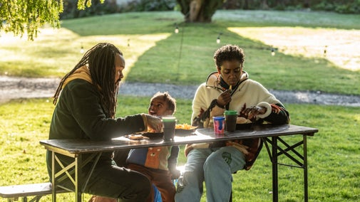 People sat on a bench eating food and drinking hot beverages in the sun